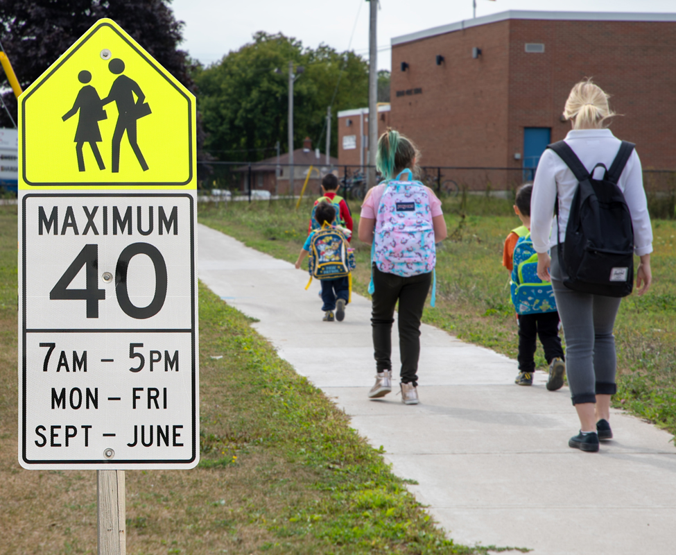 children walking along a sidewalk on their way to school and a school zone speed limit sign