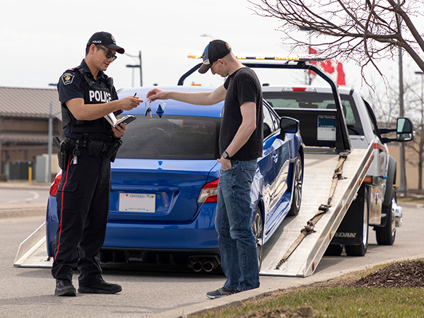 police officer taking the car keys from a driver and a car on a tow truck